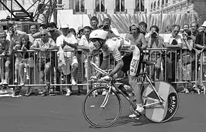Photographie en noir et blanc, d'un homme porteur d'un casque blanc, roulant sur un vélo