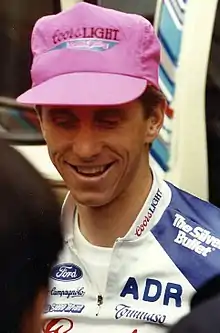 Photographie de la tête d'un homme souriant, portant une casquette rose
