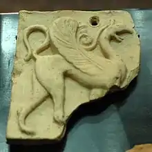 sculpture carrée endommagée au coin droit en bas : un lion avec une tête et des ailes d'oiseau
