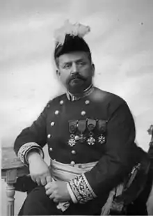 Photographie en noir et blanc d'un personnage assis en uniforme et la poitrine couverte de médailles.