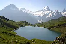 Photo d'un lac entourée de pâturages et de hautes montagnes.