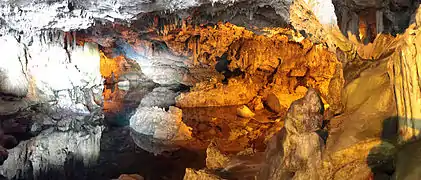 "Vue de l’intérieur de la grotte, les parois du fond se réfléchissant dans l’eau, éclairage artificiel orange"