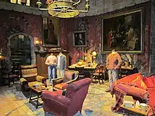 Une salle comportant des mannequins en costumes, une tapisserie rouge et des tableaux de peinture aux murs, ainsi que des gros fauteuils rouges et des tapis au sol.