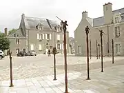 Vue d'une place, aux façades de granit, avec des statuettes surmontant des colonnes.