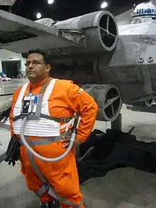 Homme déguisé en orange devant une réplique de vaisseau spatial.