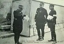 Photographie noir et blanc de trois hommes en uniforme, un lisant un document et un autre tenant un dossier dans la main.