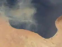 Photo satellite avec une partie de désert en bas de la photo et une partie de mer sur le haut de la photo. Le trait de côte, situé au milieu, est irrégulier et forme un renfoncement sur les terres.