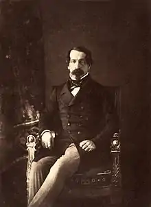 Photographie en noir et blanc de Napoléon III qui pose assis en habit civil, le regard fixé face à l'objectif.