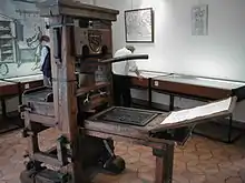 Une machine à imprimer en bois, au milieu d'une salle d'exposition avec des visiteurs.