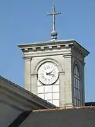 Tour rectangulaire ornée, surmontée d'une croix chrétienne. Une façade du clocher présente une horloge.