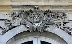 Mascaron ornant le dessus d'une fenêtre et figurant la déesse Athéna avec plusieurs attributs : casque, armure, lance, compas, équerre, longue vue, chouette, flûte, et partition
