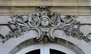Mascaron ornant le dessus d'une fenêtre et figurant le dieu Hermès avec plusieurs attributs : pétase ailé, et deux caducée