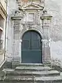 porte en bois à deux battants sous une arche portée par des pilastres. Le dessus est surmonté d'un fronton.