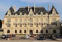 Photographie de face d'un bâtiment avec un parking devant.