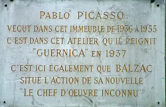 Plaque dont le texte indique : Pablo Picasso vécut dans cet immeuble de 1936 à 1955 c'est dans cet atelier qu'il peignit GUERNICA en 1937, C'est ici également que BALZAC situe l'action de sa nouvelle Le chef-d’œuvre inconnu.