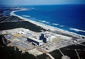 Photo aérienne couleur d'une installation industrielle au bord de la mer, sous un ciel bleu.