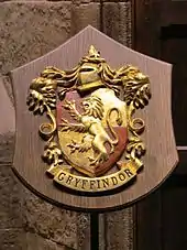 Blason représentant un lion doré et dressé, sur fond de rouge et d'or. Sous le blason est inscrit « Gryffondor » en anglais. Sur la partie supérieure du blason est dessiné un heaume