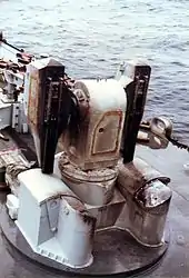 Un lanceur de missile vide à l'avant d'un navire de guerre. Il a des marques de brûlé. En arrière-plan se trouvent des douilles d'obus.