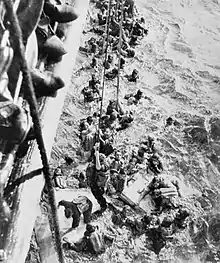Photographie prise depuis le bastingage d'un navire montrant des dizaines de marins portant des gilets de sauvetage le long de la coque.