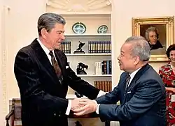  le prince, en costume bleu, serre les mains du président américain, à gauche et en costume noir