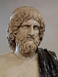 Photographie couleur d'un buste en marbre représentant un homme barbu, il porte un manteau jeté sur épaule en marbre noir.