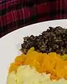 Le haggis et son accompagnement de légumes, devant le tartan du clan MacAlister.