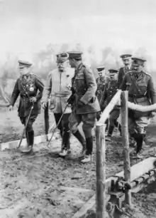 Photographie noir et blanc d'hommes en uniforme marchant sur un terrain boueux.