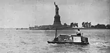 Photographie d'une voiture amphibie devant la statue de la liberté. Une femme est assise sur le toit de la voiture.