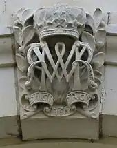 Bas-relief d'un M et d'un W entrelacés sous une couronne et au-dessus d'un ruban portant la devise « maintiendrai »