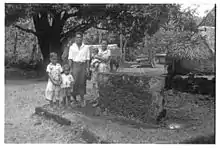 Photo en noir et blanc d'une famille composée d'un couple et trois enfants posant devant une large pierre rectangulaire