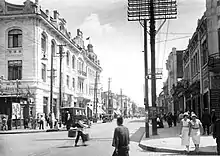 Photographie noir et blanc d'une rue avec de nombreux passant et une automobile.