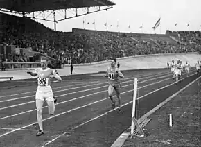 Photographie en noir et blanc de l’arrivée d'une course à pied dans un stade à huit clos.