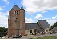 Vue latérale de l'église. A droite, le chœur et au centre , la nef, au toit surbaissé, en pierre calcaire, sont les parties les plus anciennes de l'église. Le donjon, entièrement en brique, a été construit au XVIIè siècle.