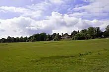 Vue d'une prairie avec au fond une construction et des arbres