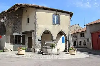 Place centrale de l'ancien village avec sa maison aux arcades et son puits