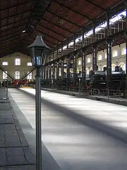 Intérieur d'un hall avec un lampadaire au premier-plan et des trains exposés aux visiteurs