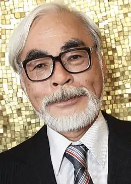 Visage de Hayao Miyazaki en costume noir et cravate bleue avec rayures.