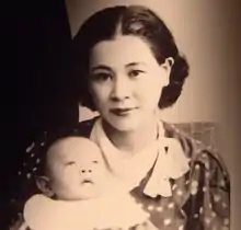 Photographie en noir et blanc d'une jeune femme avec son bébé dans les bras. La femme a des cheveux noirs et regarde la caméra.
