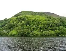 Photo présentant un plan d'eau en premier plan et une végétation dense sur des collines en deuxième-plan.