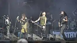 Plusieurs rockers sur une scène tiennent un micro et une guitare dans les mains.