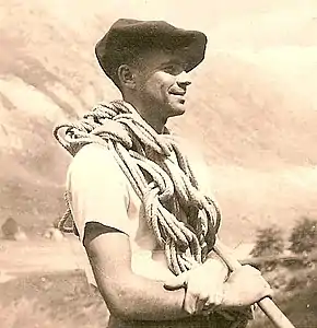 Photographie d'un homme avec un béret et une corde d'escalade.