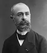 Photographie en noir et blanc d’un homme barbu et moustachu.
