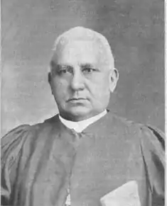 Photographie noir et blanc d'un homme blanc avec des cheveux blancs ras dans sa tenue de pasteur