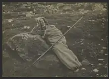 Photographie d'un homme coucher dans l'herbe, appuyé sur un rocher, enfoui dans un sac en peau d'animal.