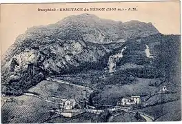 Carte postale ancienne avec quelques bâtisse, dont un château au pied d'une montagne, avec une route serpentant au milieu de vignoles.