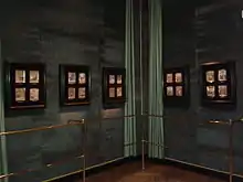 Cinq vitrines contenant les miniatures accrochées sur un mur de velours vert derrière une rambarde.