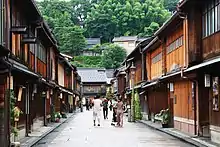 Rue dont les deux trottoirs sont surplombés par des maisons en bois à un étage.