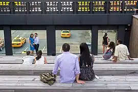 People sitting on wooden benches in a small amphitheater, which is elevated over a city street