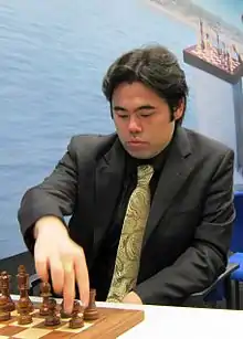 un joueur d'échecs asiatique en costume cravate s'apprêtant à toucher le pion H avec les noirs