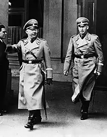 Photographie en noir et blanc de Himmler et Heydrich, vêtus d'un manteau d'uniforme, marchant l'un derrière l'autre en 1938